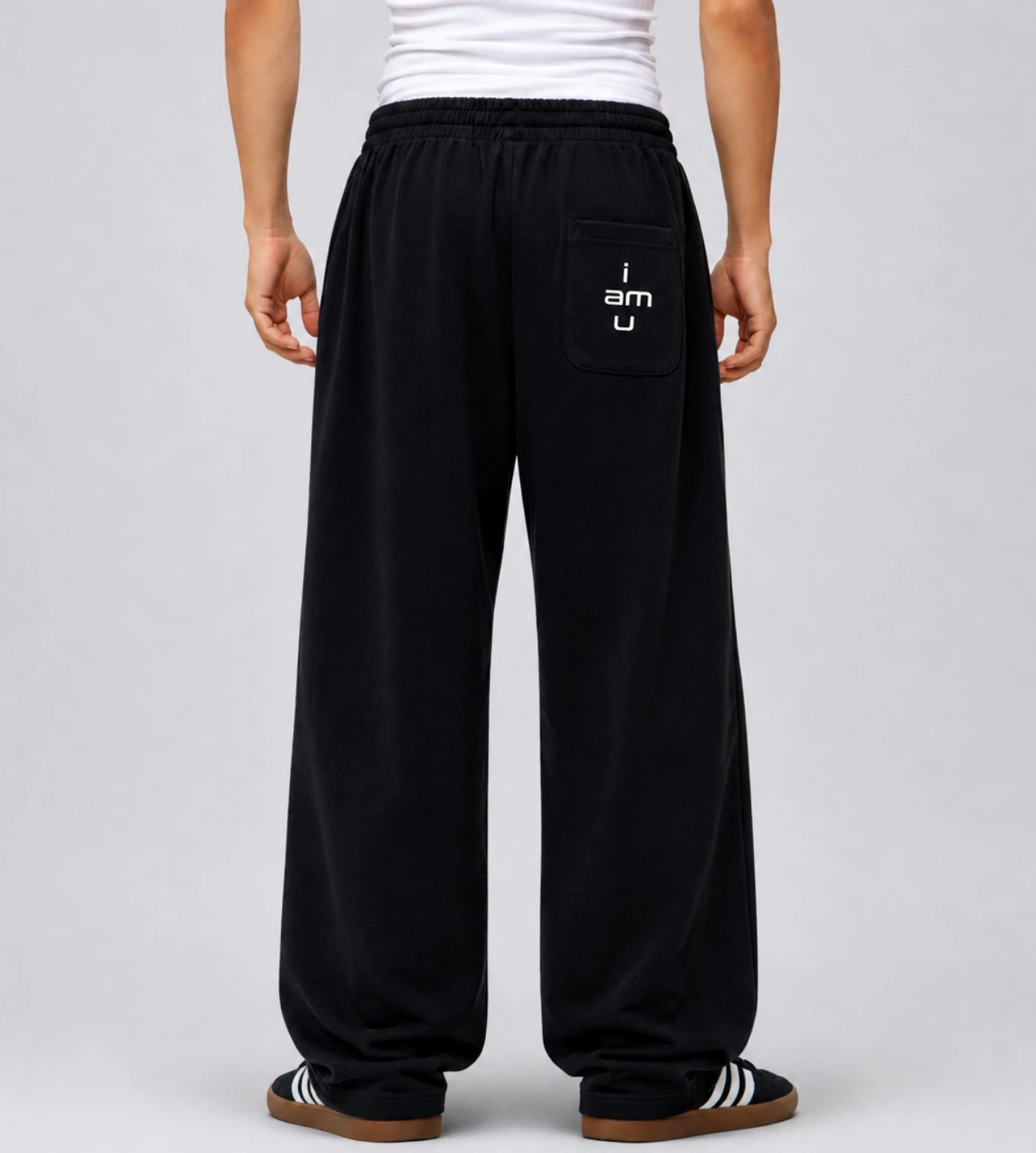 Model's back view of black curved stripe sweatpants featuring an "i am u" pocket graphic. 