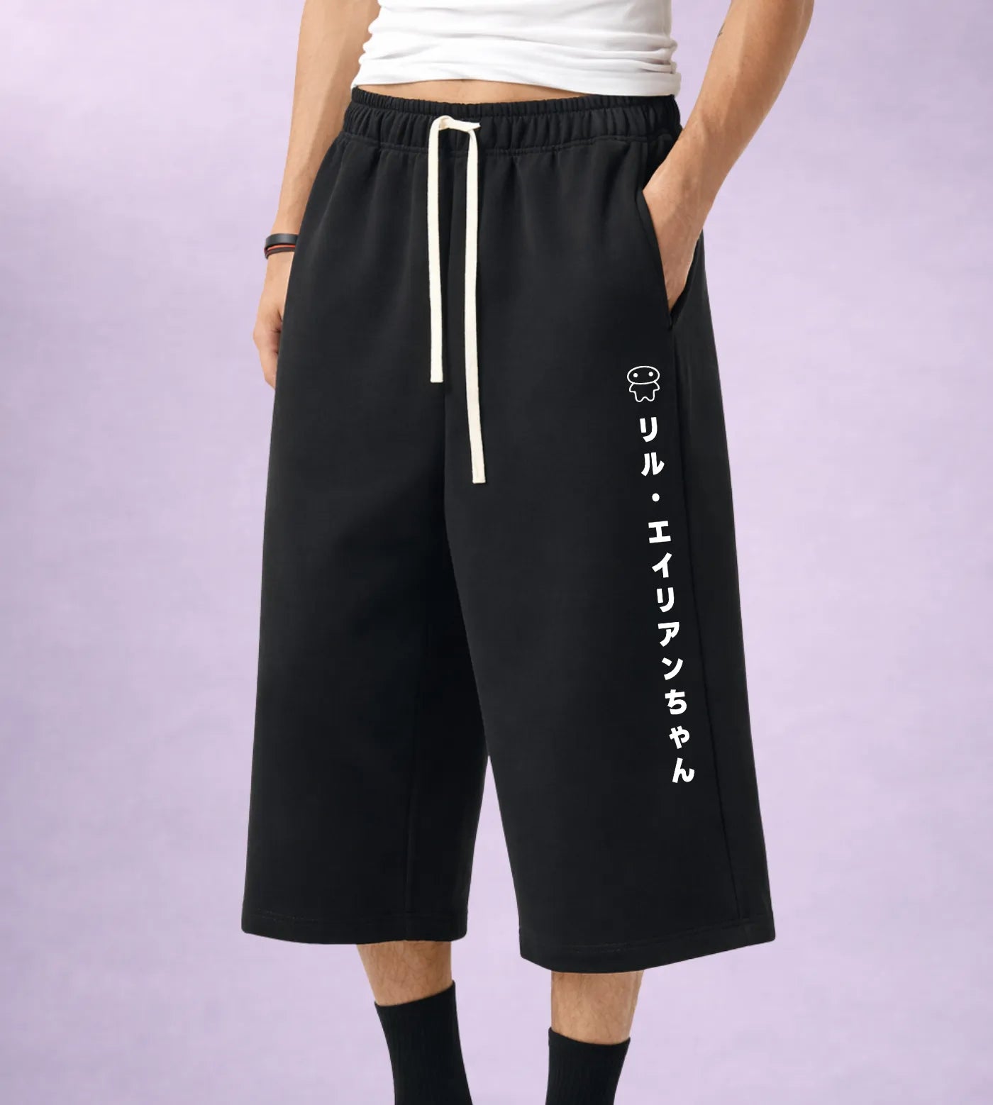 Model wears black fleece mid-length sweat shorts featuring a Japanese Lil Alien Chan graphic.  