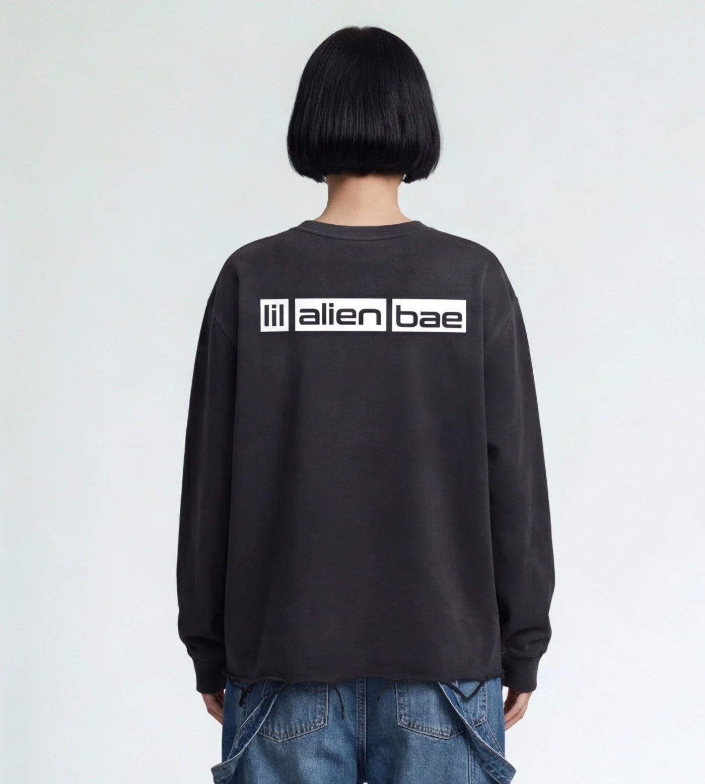Model wears a black vintage washed long sleeve shirt with raw edge hem and Lil Alien Bae back graphic.  