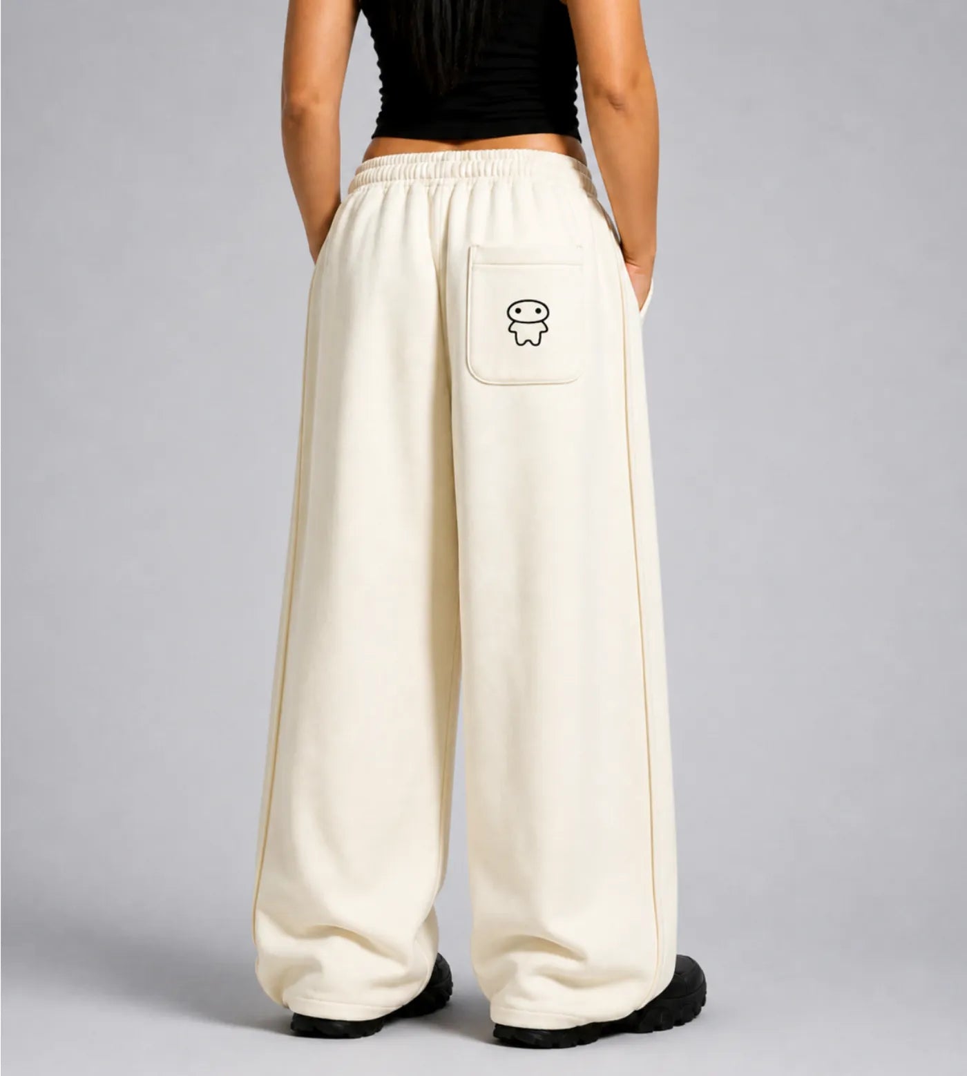 Model wears light cream straight-leg sweatpants featuring Lil Alien Bae back pocket.  