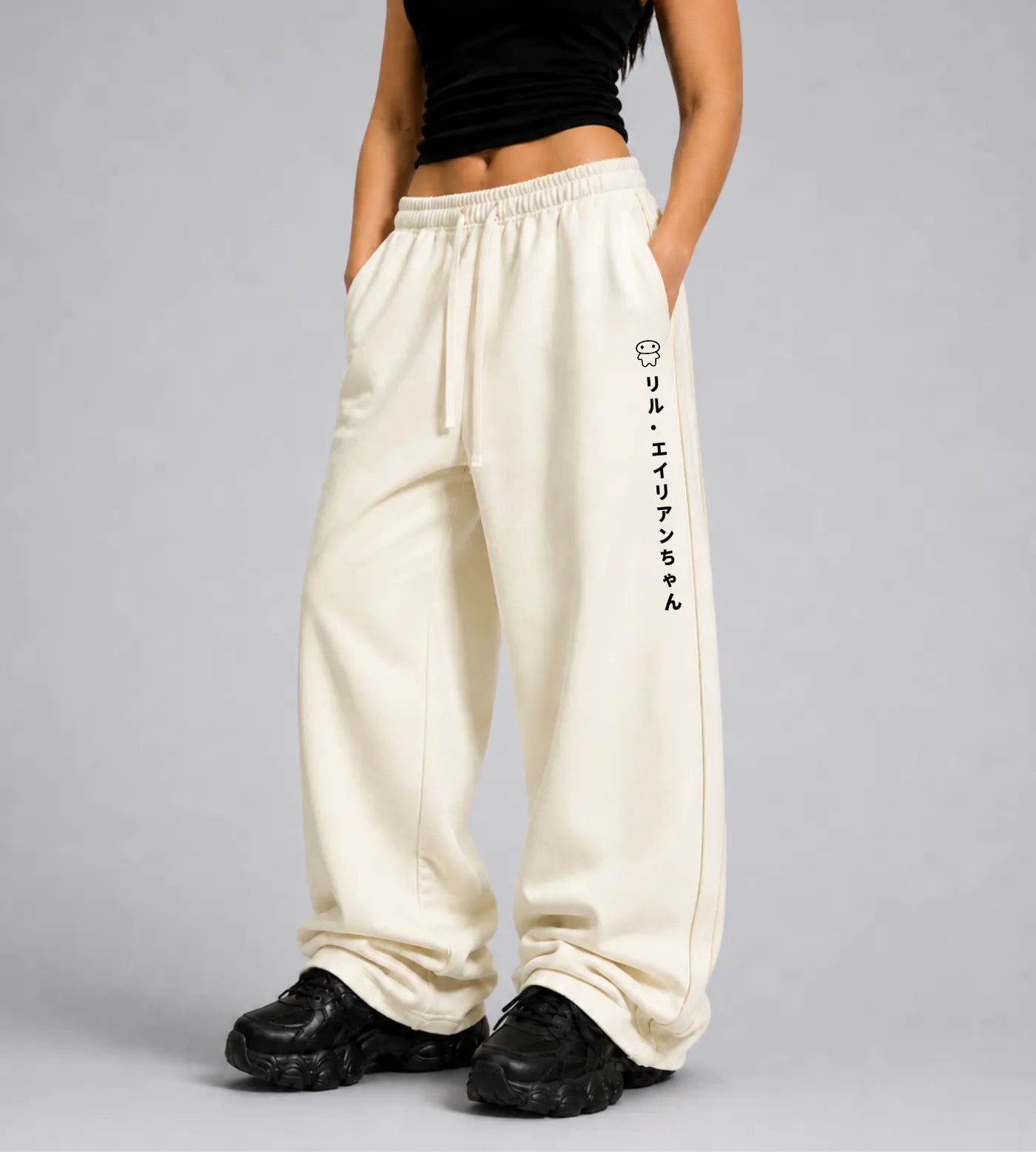 Model wears light cream straight-leg sweatpants featuring Lil Alien Bae in Japanese.  