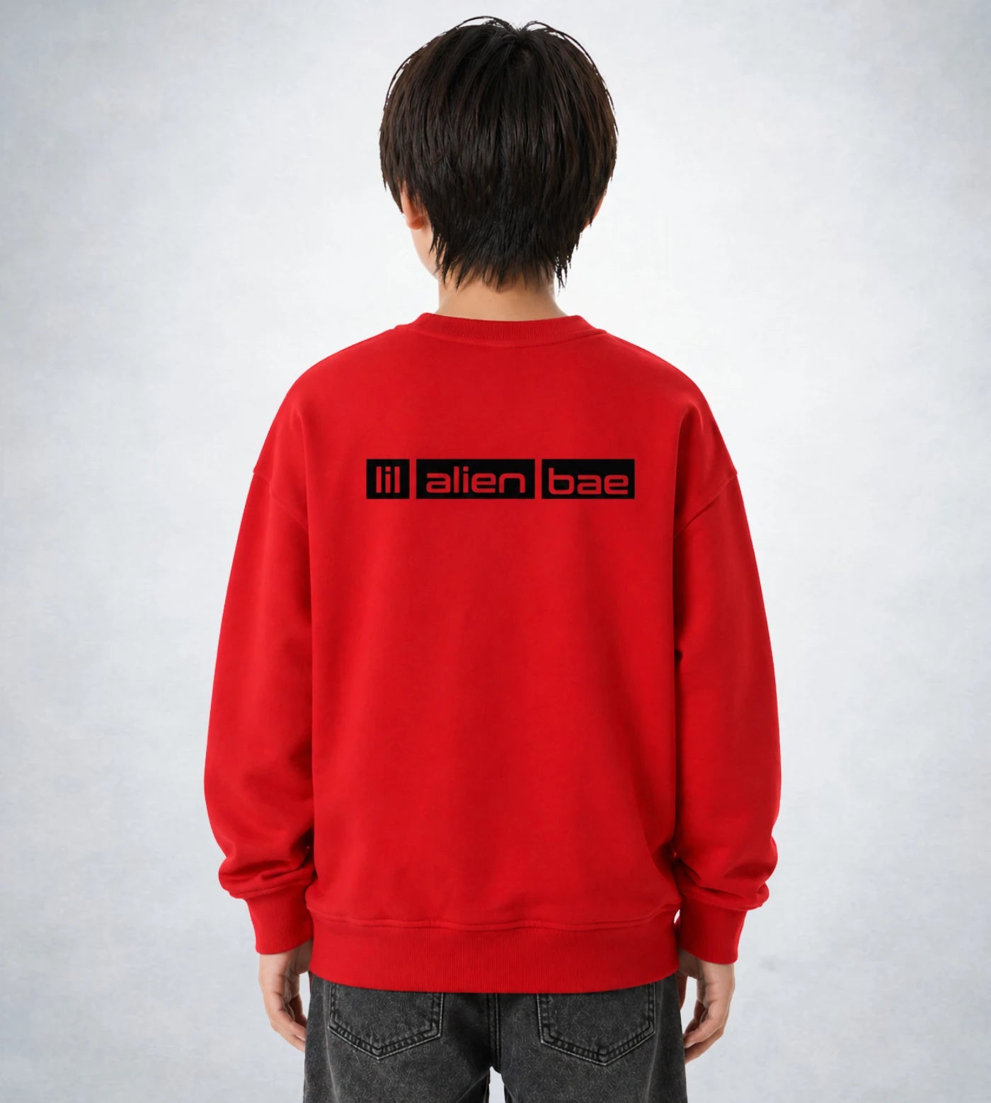 Model wears a youth red fleece sweatshirt featuring a Lil Alien Bae back graphic. 