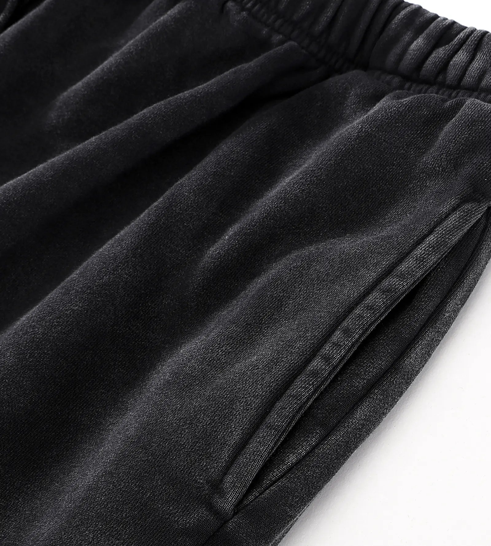 Close-up of black fabric with an elastic waistband and a side seam, photographed on a white background.