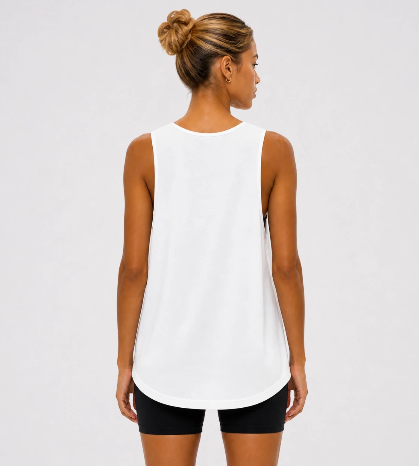 Model wears a white loose fit wide arm tank top. 