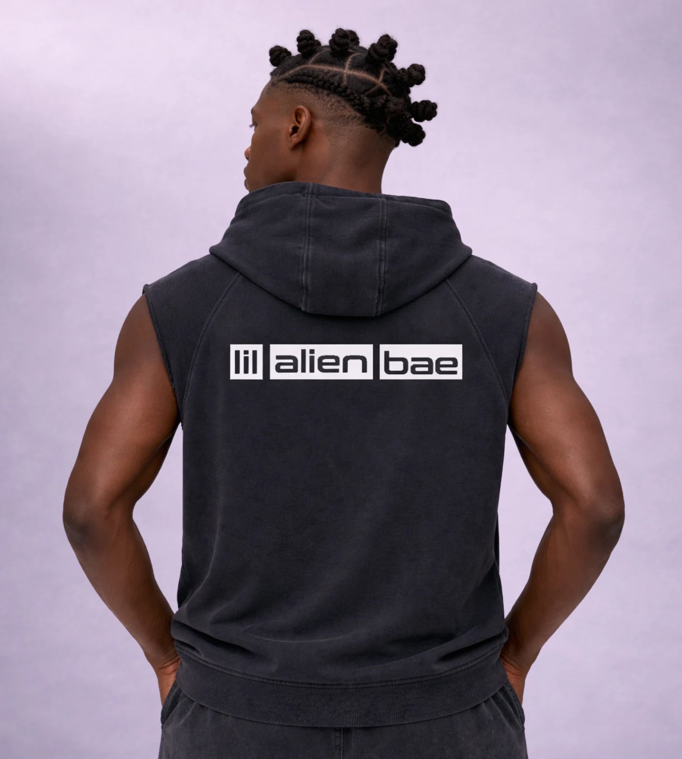 Model wears a black snow washed sleeveless hoodie featuring a Lil Alien Bae chest graphic. 