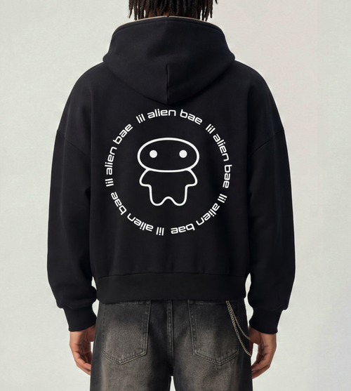 A model wears a boxy black graphic hoodie featuring a large lil alien bae logo on the back.  