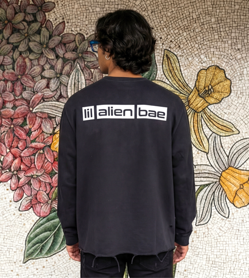 Black vintage washed long sleeve graphic shirt with ripped hem features large lil alien bae logo across the back shoulders.  